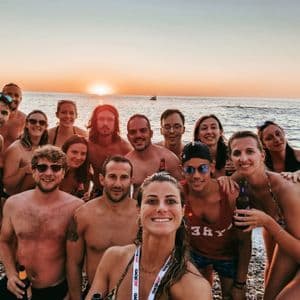Un viaggio di gruppo WeRoad scatta un selfie su una spiaggia di ciottoli al tramonto sul mare.