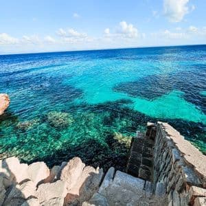 Una vista dall'alto di scale in pietra che scendono verso un mare turchese vibrante lungo una costa rocciosa.