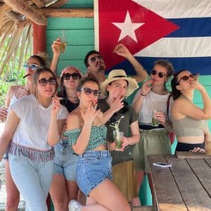 Un grupo de WeRoad posa para una foto fumando puros y bebiendo mojitos frente a una gran bandera cubana.