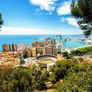 Vue aérienne d'une ville côtière avec des arènes, un grand port et la mer sous un ciel bleu.