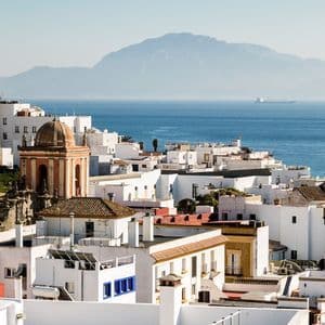 Una vista dall'alto di una cittadina costiera con edifici imbiancati affacciati sul mare e una grande montagna in lontananza.