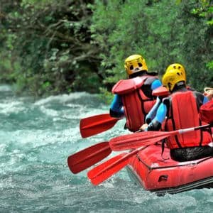 Vue arrière d'un voyage de groupe WeRoad dans un radeau rouge, faisant du rafting en eaux vives sur une rivière tumultueuse à côté d'une forêt verte.