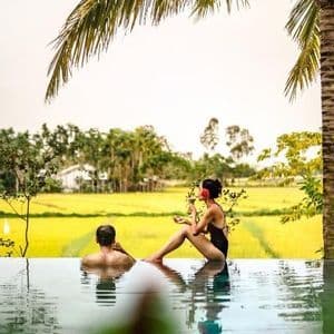 Un uomo e una donna in un viaggio di gruppo WeRoad si rilassano in una piscina a sfioro che si affaccia su una risaia di un giallo brillante.