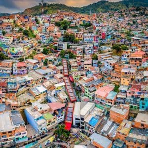 An aerial view of red outdoor escalators ascending through a densely populated, colorful neighborhood built on a steep hillside.