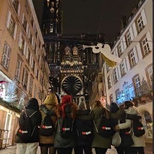 Un gruppo WeRoad si trova insieme in una strada di notte, di fronte a una cattedrale gotica illuminata con decorazioni natalizie.
