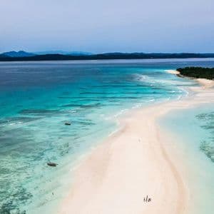 Una veduta aerea di un viaggio di gruppo WeRoad su una lingua di sabbia bianca che si protende in acque turchesi verso una piccola isola boscosa.