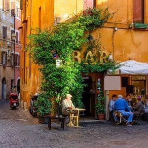 Un callejón adoquinado soleado con gente sentada en un bar al aire libre cubierto de hiedra verde exuberante.