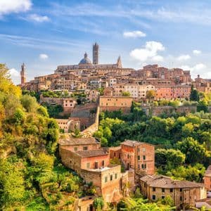 Una città storica con una cattedrale costruita su una lussureggiante collina verde sotto un cielo azzurro con nuvole bianche.
