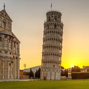 Un campanile pendente e una cattedrale ornata si ergono su un prato verde contro un tramonto dorato.