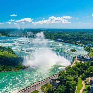 Eine Luftaufnahme eines riesigen, hufeisenförmigen Wasserfalls, der in einen türkisfarbenen Fluss stürzt und eine große Nebelwolke aufwirbelt.