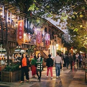 Un gruppo di persone cammina lungo una vivace via pedonale di notte, fiancheggiata da edifici tradizionali e illuminata da lanterne.