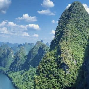 Veduta aerea di un fiume che serpeggia in una valle di lussureggianti montagne carsiche verdi, sotto un cielo azzurro con nuvole bianche.