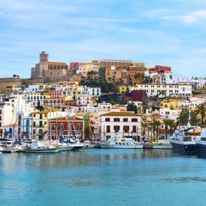 Vista dal mare di un porto con molte barche ormeggiate davanti a una colorata cittadina collinare sotto un cielo azzurro.