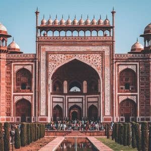 Una portería ornamentada de arenisca roja con un arco central y un estanque reflectante, con una multitud de visitantes reunidos en la entrada.