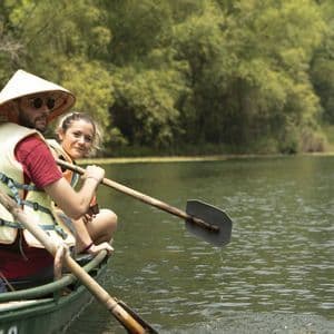 Un viaggio di gruppo WeRoad in barca su un fiume, con un uomo dal cappello conico e una donna che sorride alla macchina fotografica.
