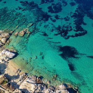 Una vista aerea di una costa rocciosa con una spiaggia sabbiosa, delimitata da acque marine limpide e turchesi.