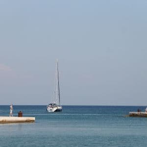 Un veliero solca le acque azzurre tra due pilastri di pietra, ciascuno sormontato da una statua di cervo in bronzo, all'ingresso di un porto.