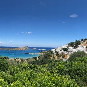Un villaggio imbiancato a calce e un'acropoli su un pendio che domina una baia turchese, con alberi verdi in primo piano.