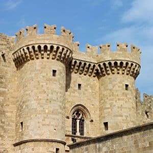Due grandi torri rotonde di un castello in pietra con merlature, sotto un cielo azzurro con nuvole leggere.