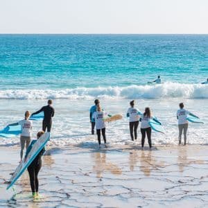 Un grupo de WeRoad con trajes de neopreno lleva tablas de surf al mar desde una costa rocosa aterrazada para una clase de surf.