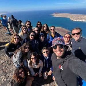 Un gruppo WeRoad si scatta un selfie da un punto panoramico elevato, con l'oceano blu e un'isola sullo sfondo.