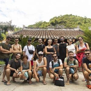 Un gruppo WeRoad posa per una foto di fronte a un edificio tradizionale con tetto in tegole, circondato da una vegetazione lussureggiante.
