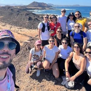 Un viaje en grupo de WeRoad se toma una selfie en una colina rocosa con vistas a una costa soleada y el océano.