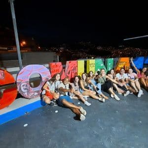 Eine WeRoad-Reisegruppe posiert nachts auf einem Dach für ein Foto, sitzend vor großen, bunten Graffiti-Buchstaben.