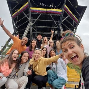 Un viaggio di gruppo WeRoad si fa un selfie energico sui gradini davanti a un'alta torre di osservazione con una bandiera colombiana.
