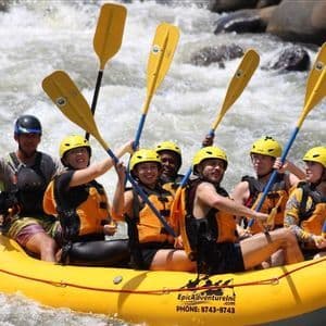 Un gruppo WeRoad sorride e alza le pagaie gialle mentre fa rafting su un gommone.