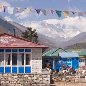 La casa de huéspedes Tengboche en un pueblo de montaña, con banderas de oración y picos nevados de fondo.
