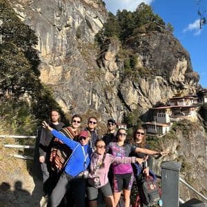Un gruppo WeRoad in viaggio posa per una foto su un sentiero di montagna, con un monastero costruito nella parete rocciosa visibile sullo sfondo.