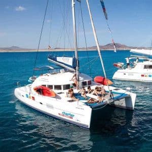 Un groupe WeRoad se détend sur le pont d'un grand catamaran blanc naviguant sur une mer bleue calme.