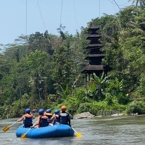 Un viaggio di gruppo WeRoad in rafting su una barca blu in un fiume, passando un tempio e una giungla lussureggiante sotto un ponte sospeso.