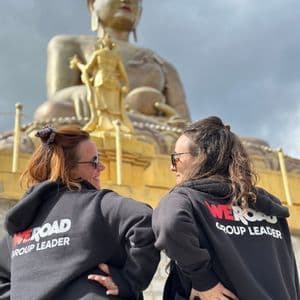 Due accompagnatori WeRoad con felpe nere con cappuccio che si sorridono davanti a una gigantesca statua del Buddha dorata.