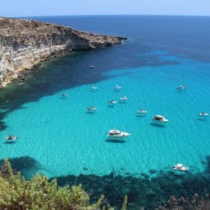 Veduta dall'alto di diverse imbarcazioni che galleggiano su acque turchesi in una baia vicino a ripide scogliere rocciose.