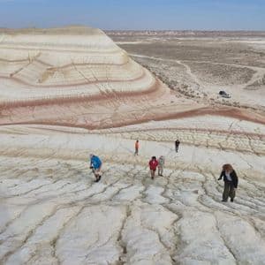 Un viaggio di gruppo WeRoad cammina su terra bianca screpolata di fronte a grandi colline a strisce colorate sotto un cielo ampio.