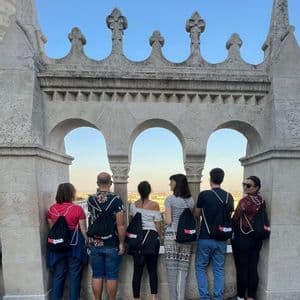 Eine WeRoad-Gruppe von hinten, die auf einem Steinbalkon mit Bögen steht und über eine Stadtlandschaft blickt.