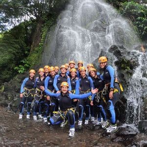 Un viaggio di gruppo WeRoad pronto per il canyoning, in posa con mute e caschi davanti a una cascata.