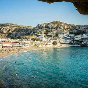 Vue depuis une grotte d'une plage animée avec des gens nageant dans l'eau turquoise à côté d'un village à flanc de colline.