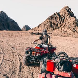 Una persona in un viaggio di gruppo WeRoad cavalca un quad rosso nel deserto con montagne rocciose sullo sfondo.