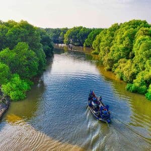 Una vista aérea de un barco con personas navegando por un río sinuoso flanqueado por densos bosques de manglares verdes.