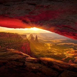 Il sole sorge su un vasto paesaggio di canyon, con la vista incorniciata dall'apertura di un enorme arco di roccia rossa.
