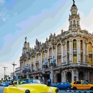 Un coche descapotable clásico amarillo está aparcado en una calle frente a un gran y ornamentado edificio histórico bajo un cielo azul.