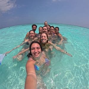 Eine WeRoad Gruppe macht ein lachendes Selfie beim Schwimmen im klaren, türkisen Meerwasser.