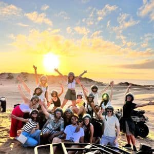 Un viaggio di gruppo WeRoad sorride e posa con i quad sulle dune di sabbia al tramonto.