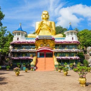 Eine riesige goldene Buddha-Statue thront auf dem kunstvollen Goldenen Tempelgebäude. Treppen führen zu einem großen Eingang, der einem Monsterschlund gleicht.