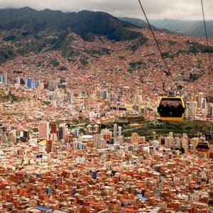 Vista aérea de teleféricos amarillos viajando sobre una ciudad densamente poblada con edificios de tejados de terracota a la base de una gran montaña.