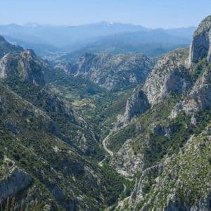 Una vista panorámica de un valle profundo que serpentea a través de una cadena montañosa escarpada y arbolada bajo un cielo azul claro.