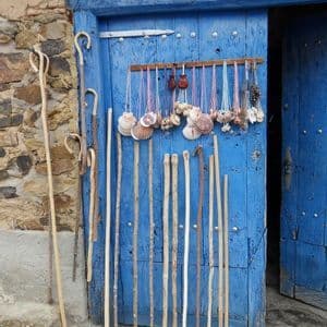 Bastones de madera y collares de conchas de vieira se exhiben sobre una puerta de madera azul brillante en una pared de piedra.